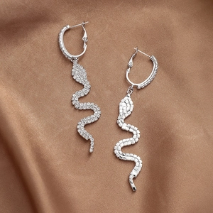 Detailed view of silver snake drop earrings with sparkling rhinestones on satin fabric