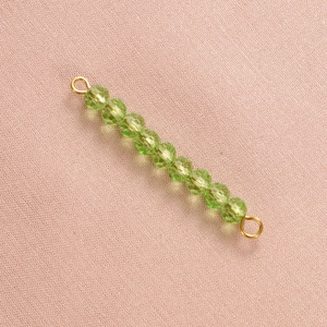 Macro shot of green faceted crystal beads with golden metal connectors on pink fabric