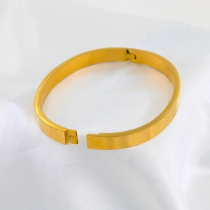 Macro detail of golden oval bangle with hinge closure on white silk background