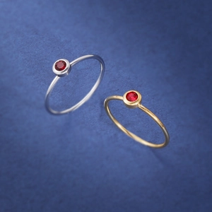 Close-up of gold and silver minimalist rings with round red birthstone bezel setting
