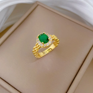 Macro detail of gold watch-band style ring with oval emerald and diamond halo