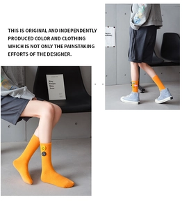 Close-up of bright orange ribbed cotton mid-calf socks with round smiley face patches