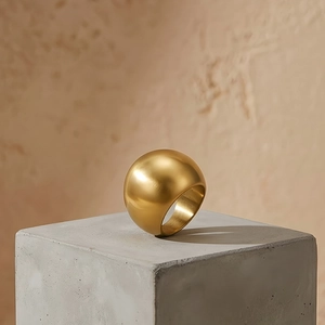 Close-up of a wide gold stainless steel dome ring displayed on a concrete block