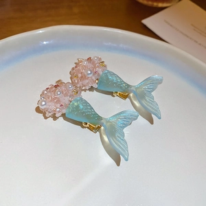 Detailed shot of mermaid tail earrings with blue resin and pearls in a ceramic dish