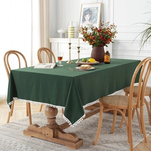 Modern dark green cotton tablecloth with white pom-pom fringe in a home dining setting
