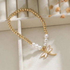 Detail of 18K gold plated beaded bracelet with pearls and a dragonfly pendant on jewelry box