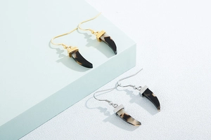 Détail de boucles d'oreilles en corne, finitions or et argent avec texture marbrée