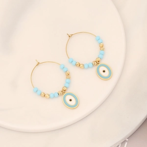 Close-up of golden hoop earrings with blue beads and enamel evil eye charms on white ceramic