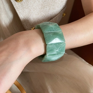 Detail of a wide fruit green acrylic bracelet with white marble texture on a woman's wrist