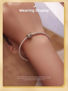 Close-up of a silver mesh bracelet featuring an intricate hollow heart charm with gold accents