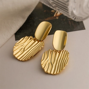 Detail shot of gold heart earrings with artistic corrugated texture on soft fabric