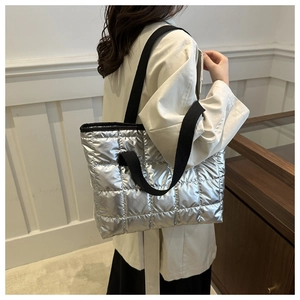 Quilted silver metallic tote bag featuring black woven straps on model's shoulder