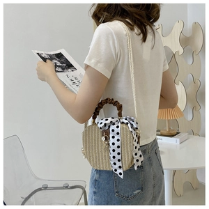 Detail of woven straw bag with polka dot ribbon and pleated handle held by model