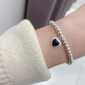 Silver bead bracelet with black heart pendant worn on wrist with cream knit sweater
