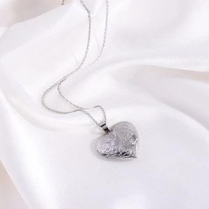 Vue détaillée d'un collier médaillon en forme de cœur gravé sur fond de soie blanche
