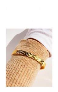 Dettaglio del bracciale rigido dorato a strisce verticali su manica in maglia