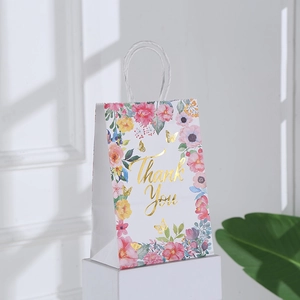 Detail showing elegant white kraft gift bag with floral patterns and gold foil Thank You text