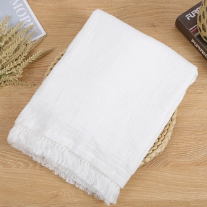 Detailed texture of white cotton muslin baby blanket with elegant tassel edges on a table