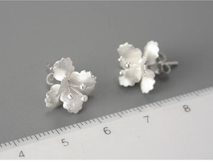 Detailed macro shot of 925 silver flower stud earrings showing matte texture and size scale
