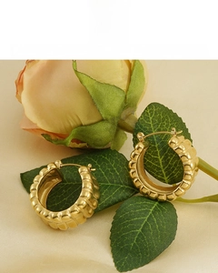 Détail de boucles d'oreilles créoles dorées 18 carats avec texture sur tissu en soie