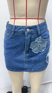 Detailed close-up of blue denim skirt featuring raw-edge floral patchwork and silver buttons