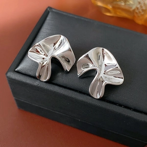 Macro view of irregular silver metal stud earrings with abstract folded mushroom design