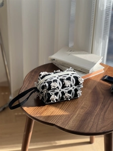 Detail of black canvas pouch with white geometric embroidery and zipper on wooden table