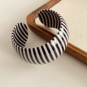 Detail of wide open bangle with black and white stripes on a textured fabric display