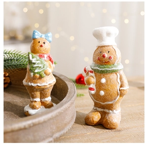 Festive resin gingerbread man and girl figurines on a rustic wooden tray with warm lighting