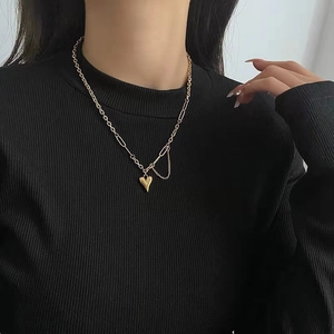 Collana dorata con ciondolo a cuore e nappe asimmetriche su maglia nera