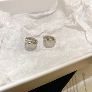 Detail view of silver square hoop earrings placed in a white jewelry box on pleated paper