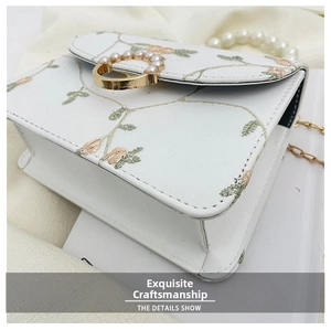 Close-up of white floral embroidery bag with pearl handle and golden ring buckle detail