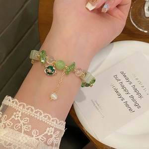 Detailed view of adjustable planet bracelet with green stones and pearl on lace cuff