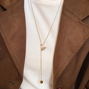 Detail of a gold Y-shaped necklace with tiger eye beads on a model wearing a white knit