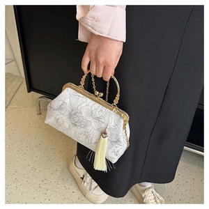 Detail of floral embroidery, golden metal handle, and fringe tassel on white shell bag