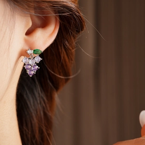 Close-up of a grape-shaped dangling earring with purple and green crystals on a model