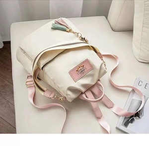Detail of a creamy white nylon backpack featuring pink straps and a rabbit label