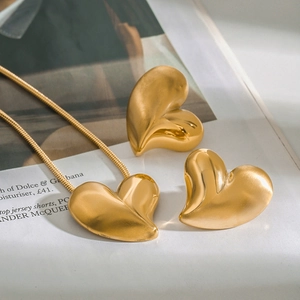 Detailed view of matte brushed gold heart necklace and earrings on a magazine background