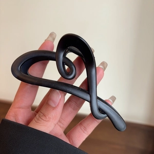 Close-up of a matte black heart-shaped hair claw clip held in hand for detail