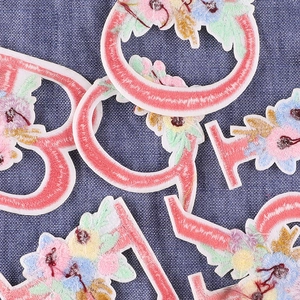 Pink floral alphabet embroidery patches with colorful flowers on blue denim base