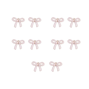 Close-up of eight pink enamel bow charms with gold metal borders for DIY jewelry