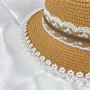 Close-up of handmade straw hat featuring delicate white lace trim and striped decorative band