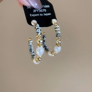 Dettaglio degli orecchini a C con perle di marmo e perle bianche su un cartoncino nero