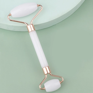 Macro shot of dual-head white jade facial roller with rose gold metal bracket detail