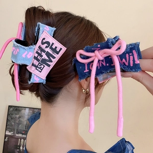 Detail of denim bow hair claw clips with pink text and frayed edges on female model
