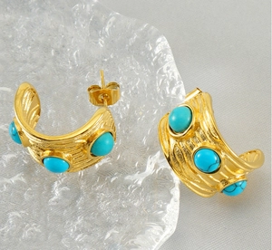 Vue macro de boucles d'oreilles dorées texturées en C serties de turquoise sur verre
