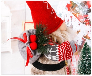Detail of Christmas gnome with red hat and reindeer knit sleeves beside a tree