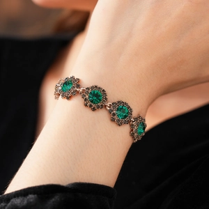 Close-up of vintage bracelet featuring a green gemstone floral clasp on a metal band