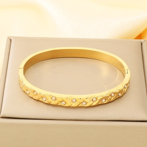 Detailed close-up of 18K gold-plated bangle with sparkling crystals on champagne silk fabric