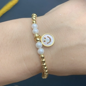 Detail of beaded bracelet with gold metal beads, white pearls and mother-of-pearl smiley face